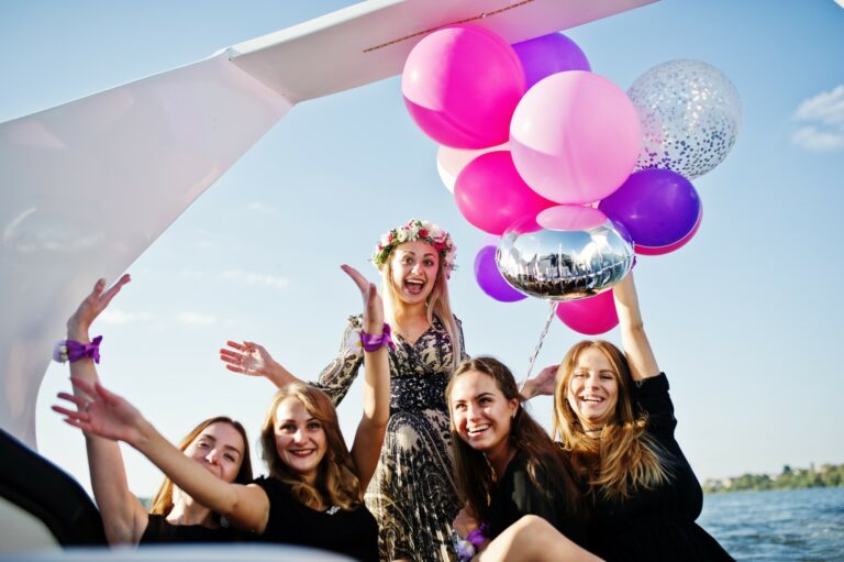 A group of women on a boat celebrating a bachelorette party with colorful balloons.